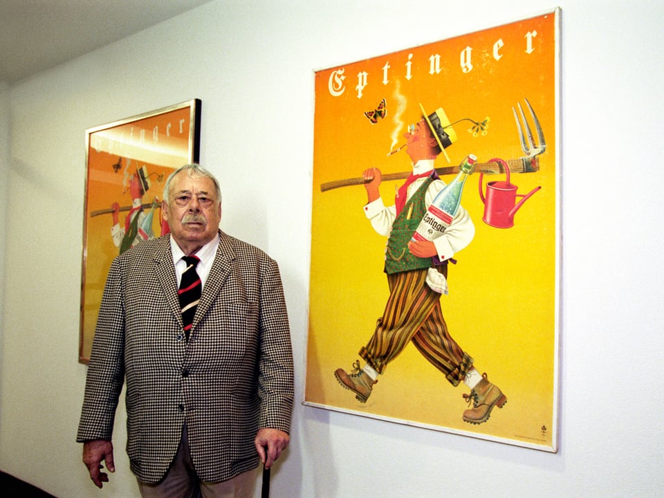 Der Künstler Herbert Leupin posiert in einer Ausstellung vor einem seiner Plakate.