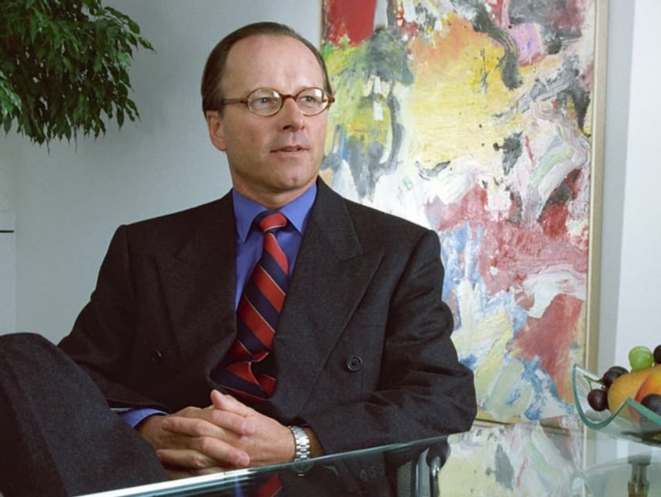 Stephan Schmidheiny sits in a chair with his legs crossed, office interior can be seen behind him