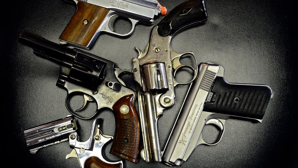 Drei Revolver und zwei Pistolen liegen zusammengewürfelt auf einem Tisch.