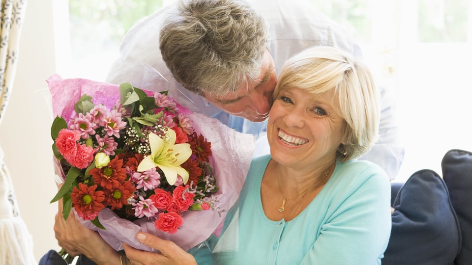 Ein Mann schenkt einer Frau einen Blumenstrauss und küsst sie auf die Wange