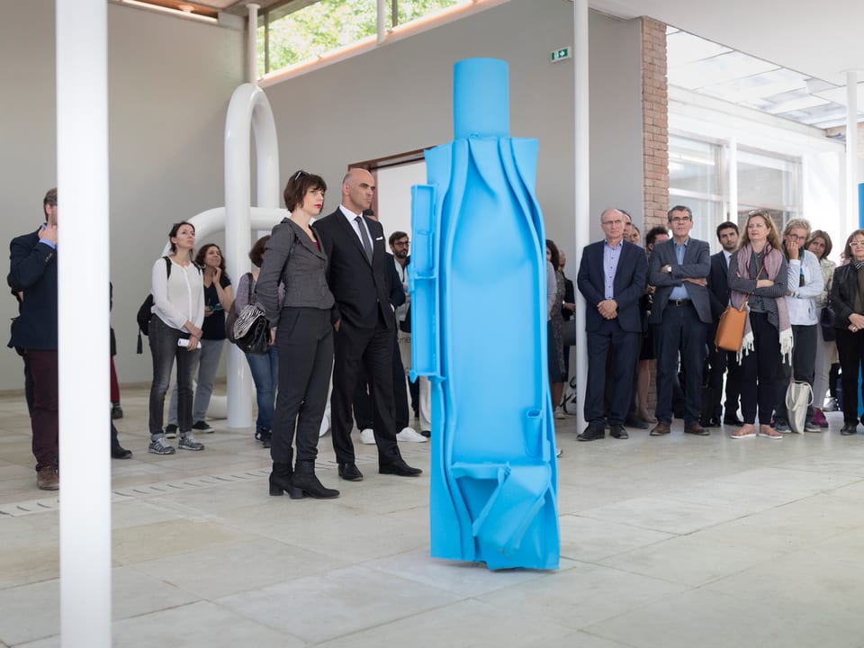 Eine blaue Skulptur steht in einem hellen Raum und wird von Leuten betrachtet.