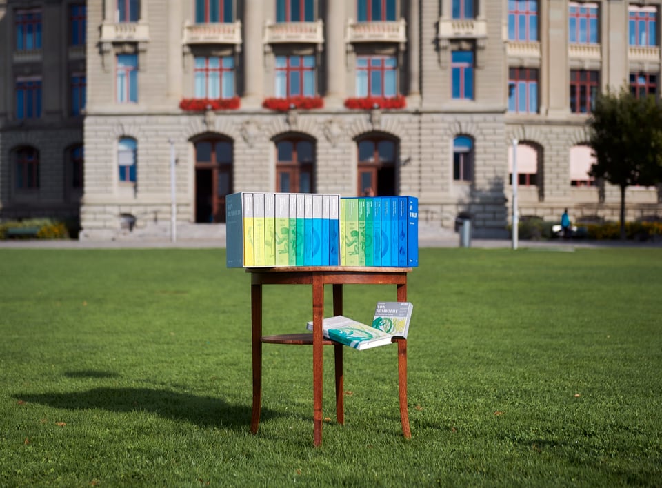 Auf dem Foto sind alle Bände der gesammelten Schriften zu sehen, im Hintergrund das Hauptgebäude der Uni Bern.