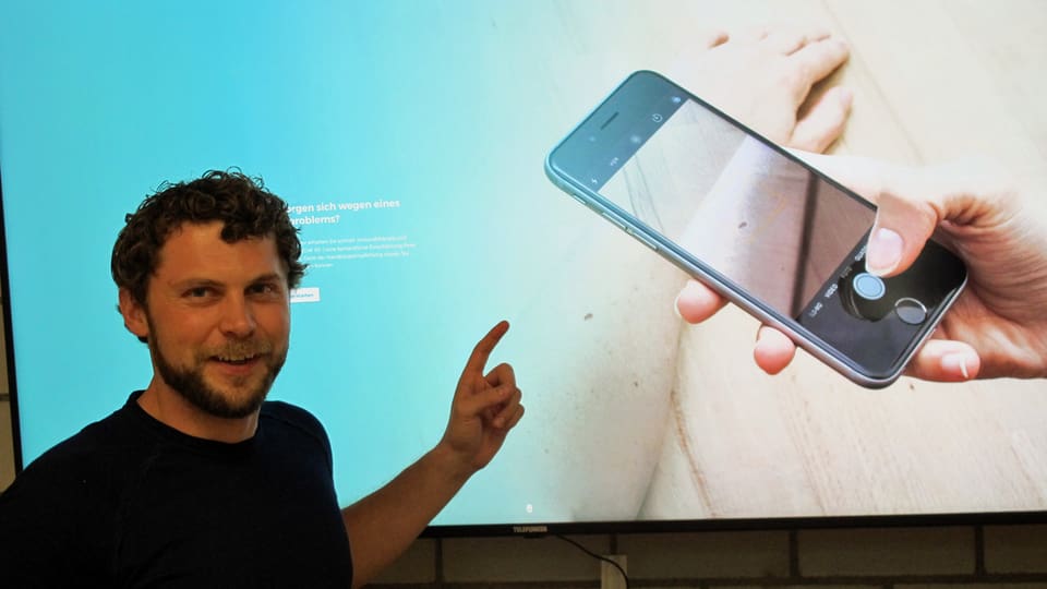 Tobias Wolf vor einer Leinwand, wo ein Handy zu sehen ist.