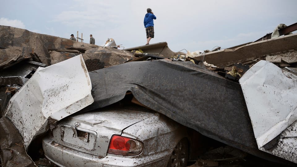 Ein Junge steht auf einem Trümmerhaufen, das Heck eines silbernen Autos schaut heraus.