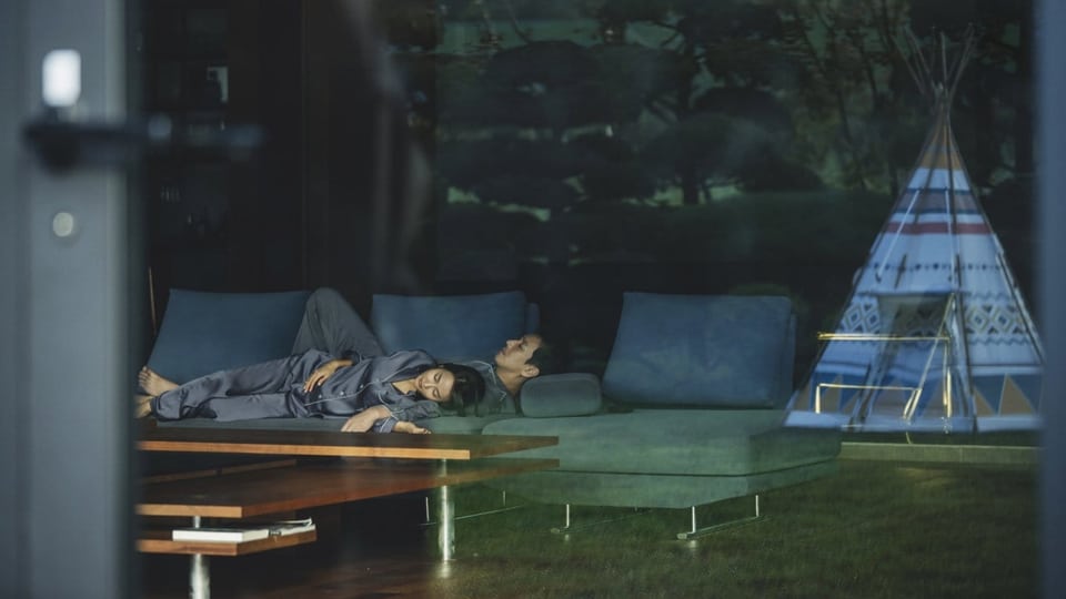 Ein Mann und eine Frau schlafen auf einem Sofa in einem geräumigen zimmer, im Hintergrund ein Tipizelt.