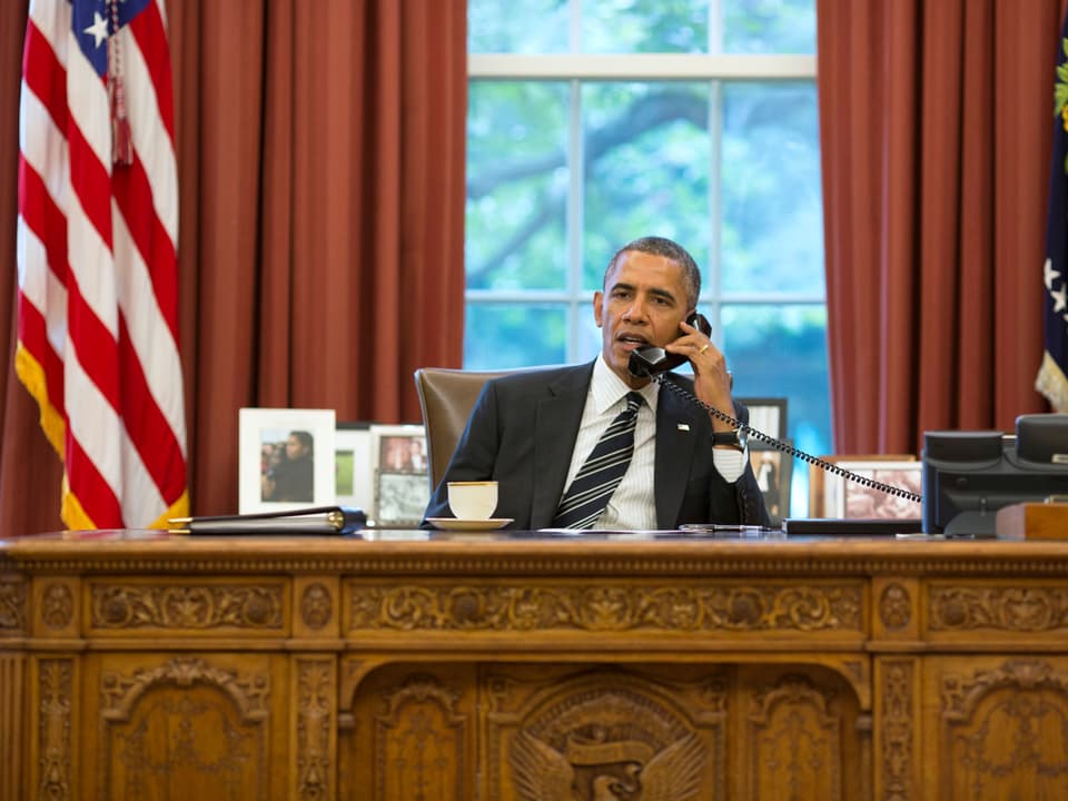 Barack Obama sitzt an einem Tisch und telefoniert.