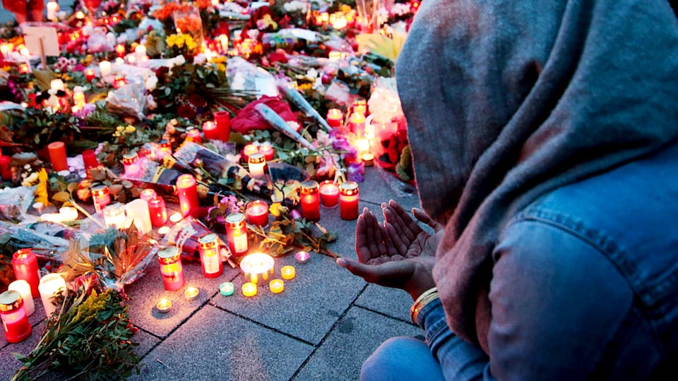 Eine junge Frau sitzt mit Kapuzze und gefalteten Händen nach dem Amoklauf in München vor Kerzen und Blumen.