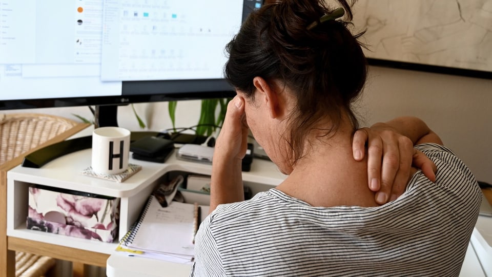 Eine Frau vor einem Computer hält sich mit der einen Hand die Stirn und mit der anderen ihren Nacken. 