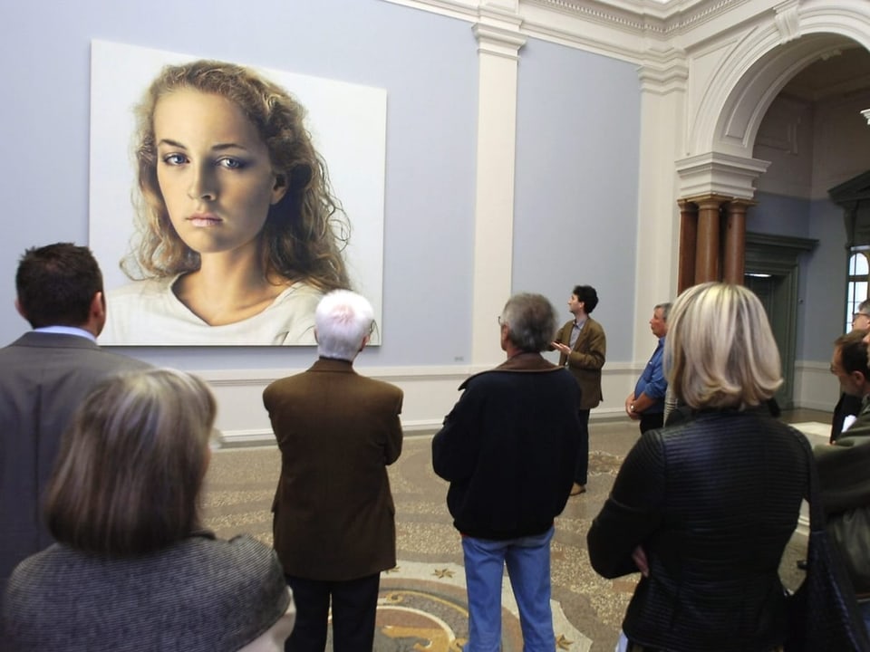 Visitors look at paintings of a woman