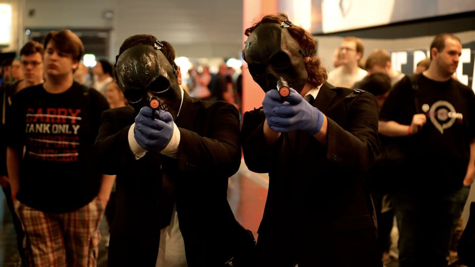 Zwei Männer in schwarzen Totenkopf-Masken und Gummihandschuhen ziehen ihre Pistolen.