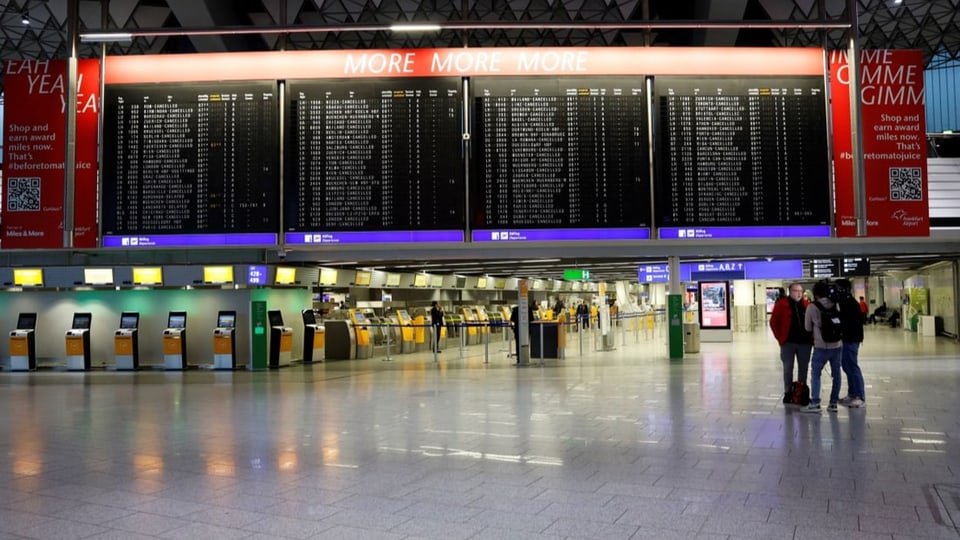 Grosse schwarze Anzeigetafel auf denen fast überall «cancelled» steht. Darunter stehen drei Personen.