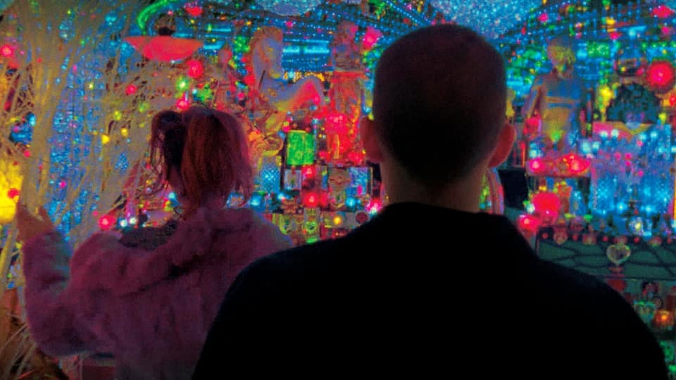 Zwei Menschen in einem Raum mit farbigen Lichtern.