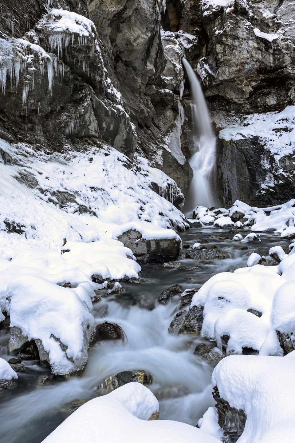 Das Bild zeigt eine kleinen Wasserfall inmitten einer Schneelandschaft. 