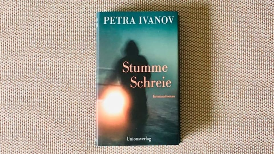 Krimi Nummer 5 «Stumme Schreie» von Petra Ivanov liegt auf einem beigen Sofastoff