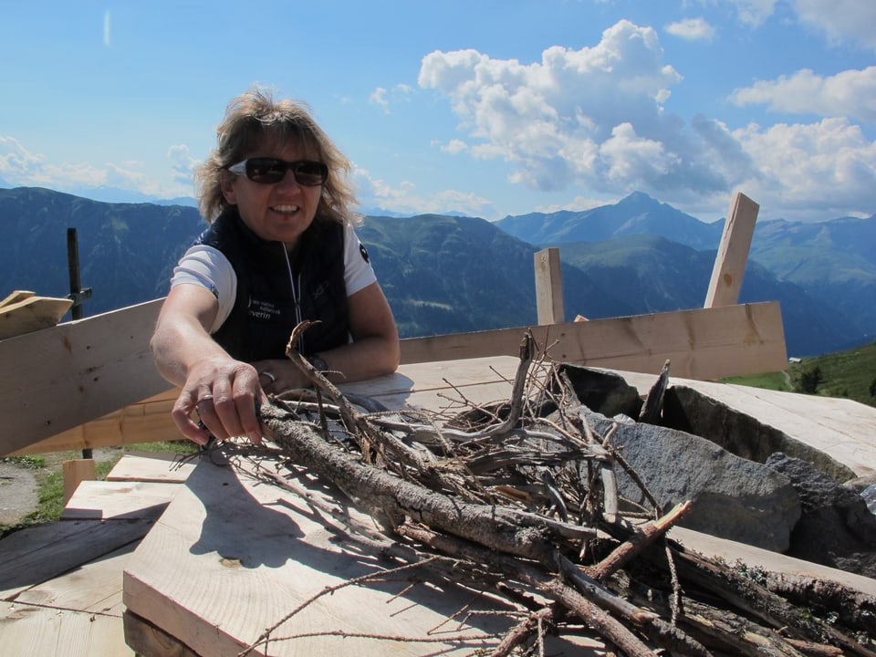 Eine Frau sitzt auf einer Holzkonstruktion, umgeben von einer alpinen Landschaft