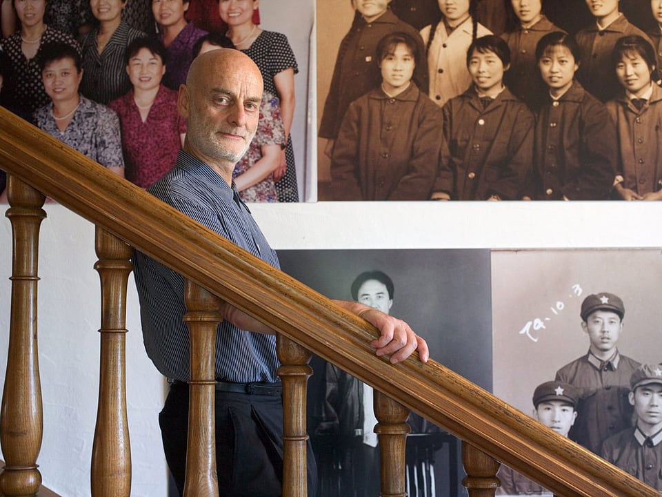 Uli Sigg steht auf einer Treppe - im Hintergrund hängen Fotografien an der Wand.