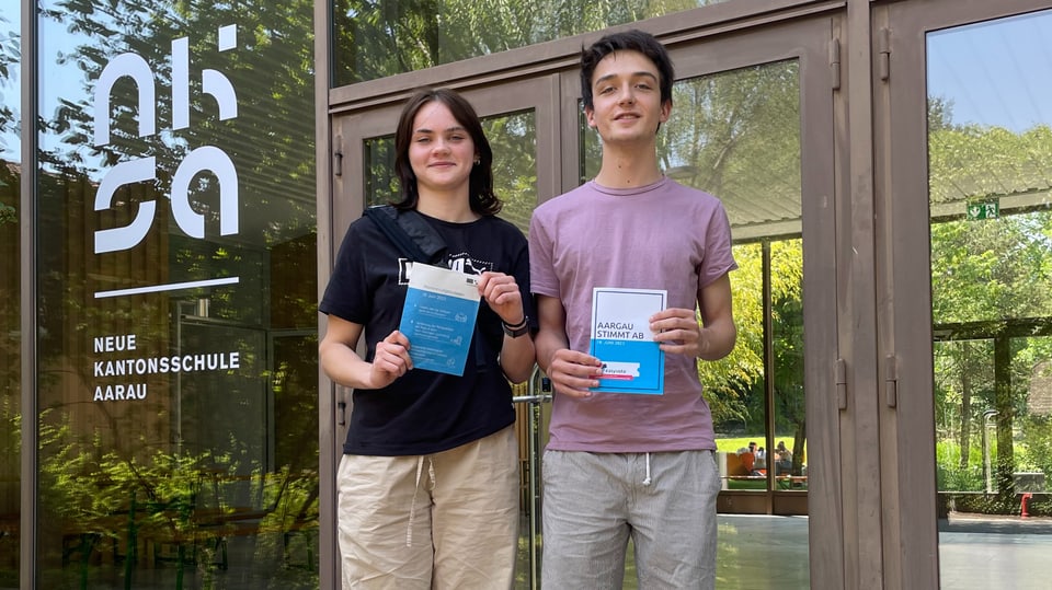 Junge Frau und und junger Mann vor Kantonsschule mit Abstimmungsbüchlein in der Hand