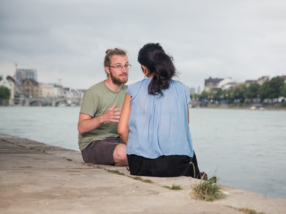 Eine Frau und ein Mann unterhalten sich am Ufer des Rheins.