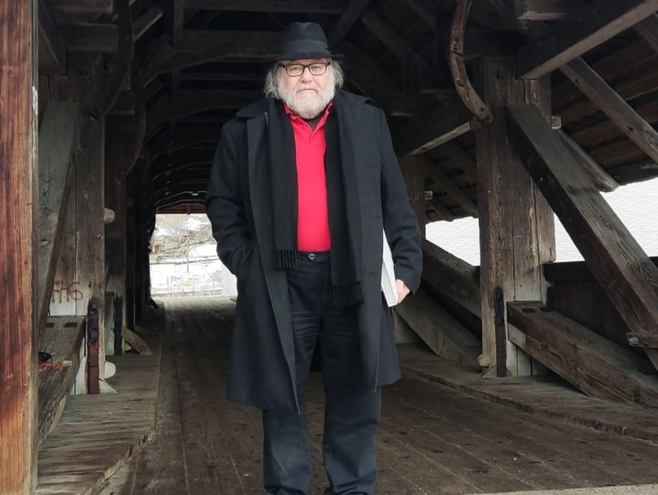 Mann mit Mantel und Hut auf einer Holzbrücke.