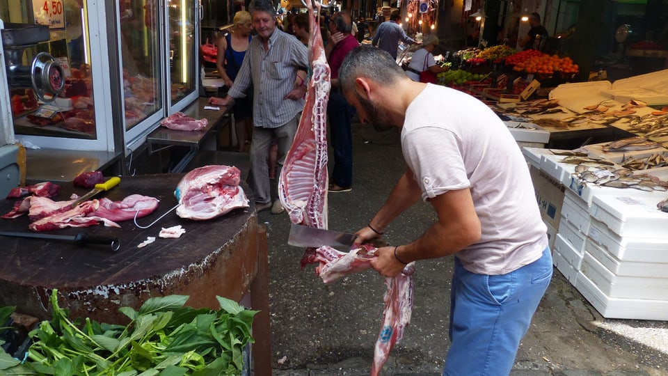 Ein Metzger schneidet ein Stück Fleisch von einer Lammhälfte.