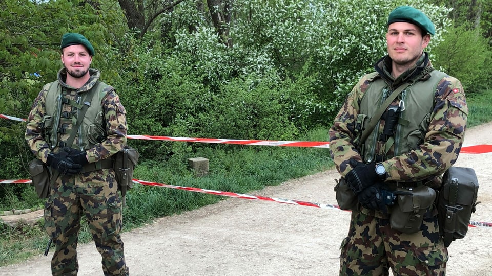 Zwei Soldaten im Tarnanzug vor einem Absperrband.