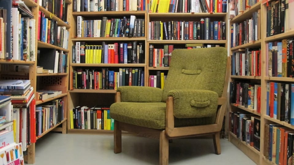 Olivfarbener Sessel zwischen vollen Bücherregalen.