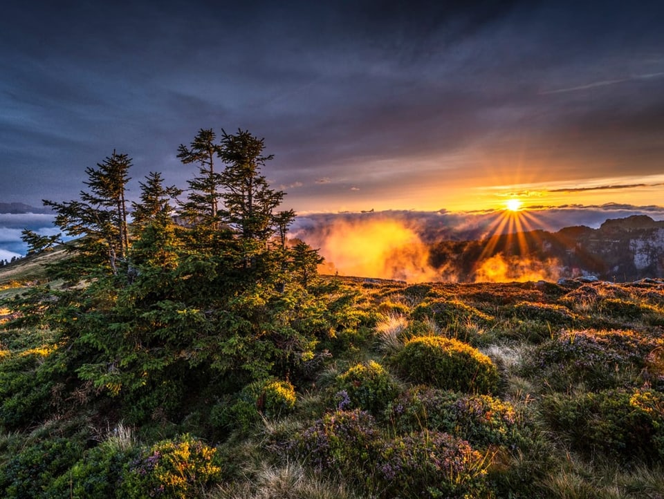 Sonnenuntergang in den Bergen mit Nebelschwaden in den Tälern und dunklen hohen Wolken. 