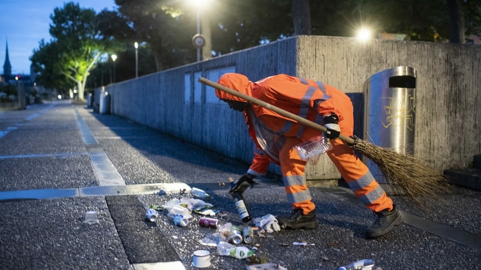 Ein Mann mit oranger Kleidung sammelt Abfälle vom Boden auf.
