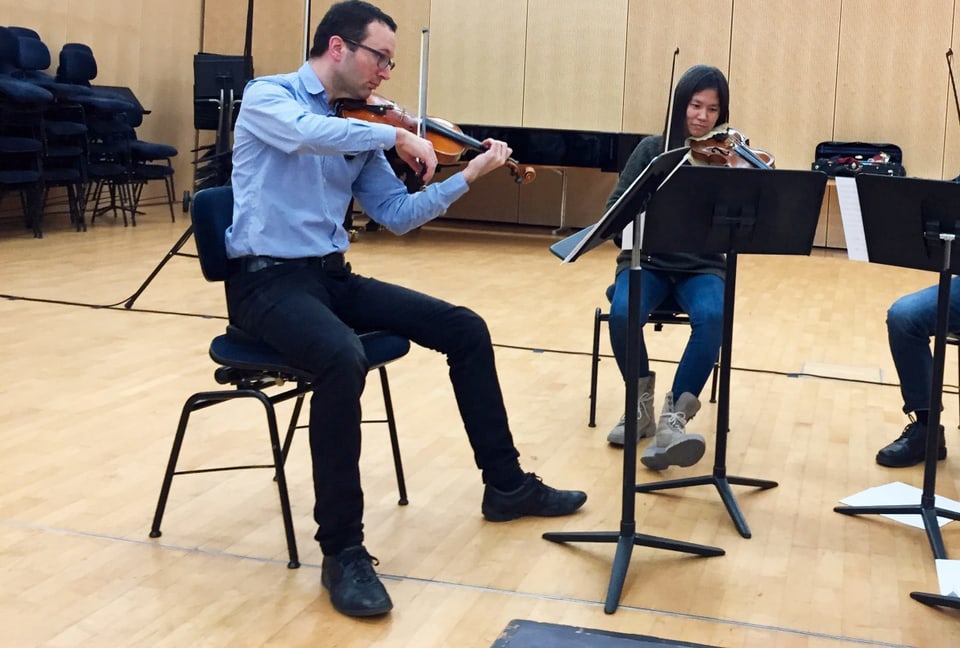 Zwei Männer und eine Frau in einem grossen Raum. Sie spielen auf ihren Geigen und Bratschen.