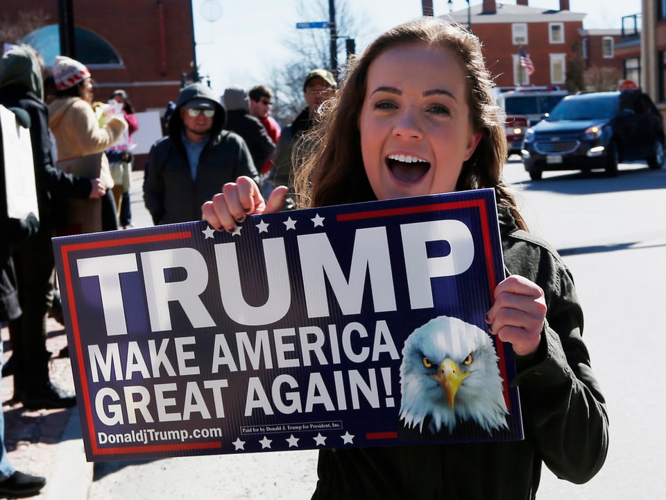 Junge Frau hält ein Schild, worauf steht: Trump macht Amerika wieder grossartig.