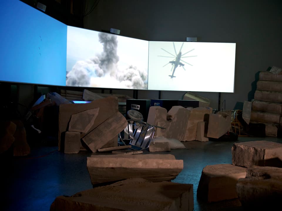 Videoscreen, dreiflügelig mit Projektionen: Helikopter, Detonation, Himmel