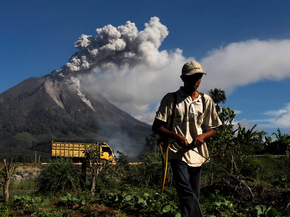 Ein Mann flieht aus einem der Dörfer rund um den Mount Sinabung. Im Hintergrund ist der Asche speiende Vulkan zu sehen. (reuters)