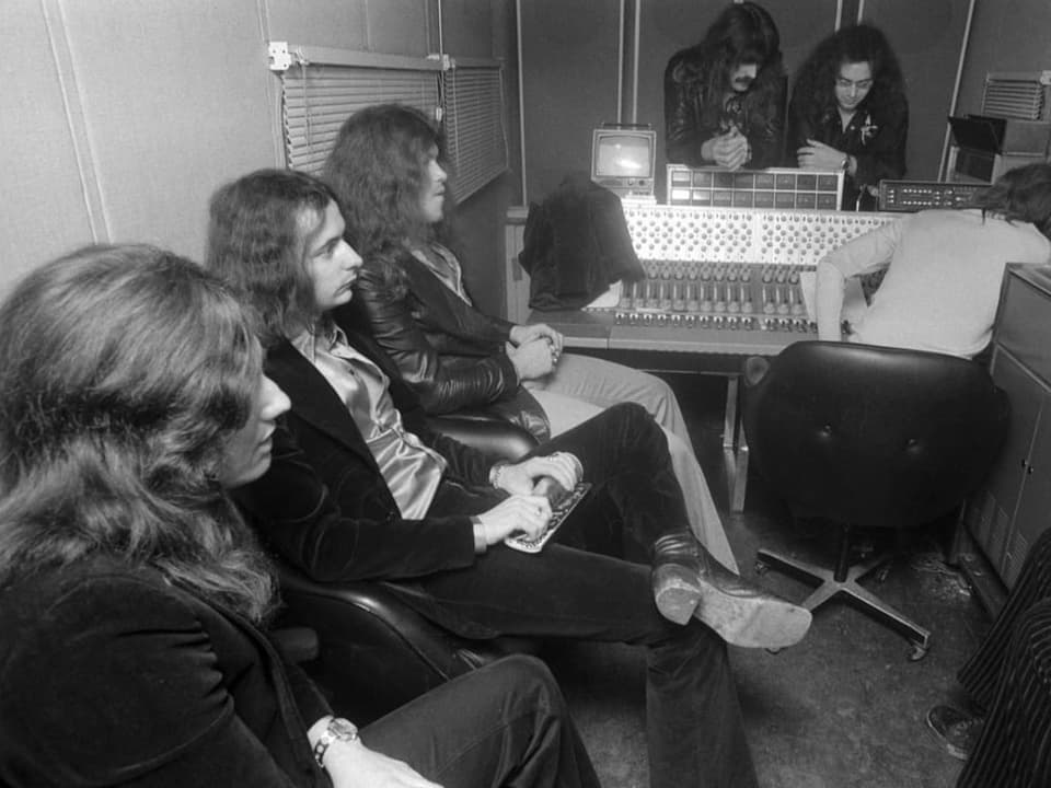 Schwarzweissaufnahme: Bandmitglieder mit langen Haaren sitzen im Aufnahmestudio