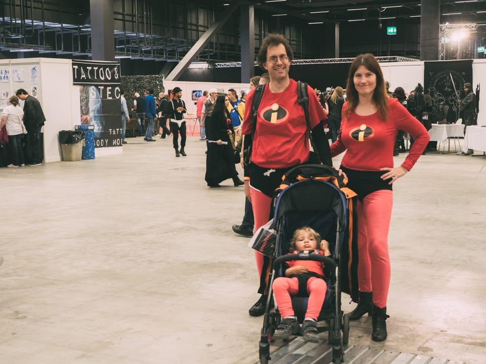 Eltern schieben als Incredibles verkleidet einen Kinderwagen 