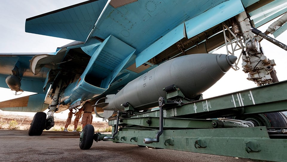 Eine Bombe wird unter den Flügel eines russischen Kafflugzeugs geschoben. 