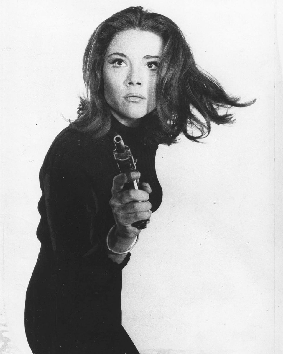 Altes Foto einer Frau in schwarzem, engem Anzug und mit einer Pistole in der Hand.