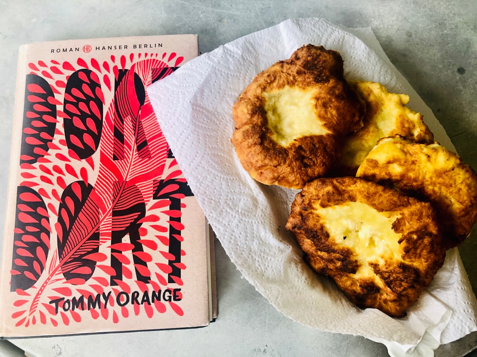 Neben dem Roman «Dort Dort» von Tommy Orange steht ein Teller mit selbstgemachtem Fry Bread. 