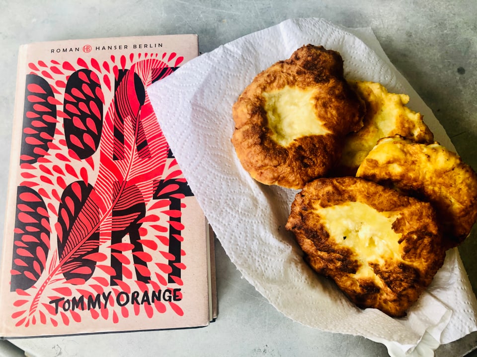 Neben dem Roman «Dort Dort» von Tommy Orange steht ein Teller mit selbstgemachtem Fry Bread. 