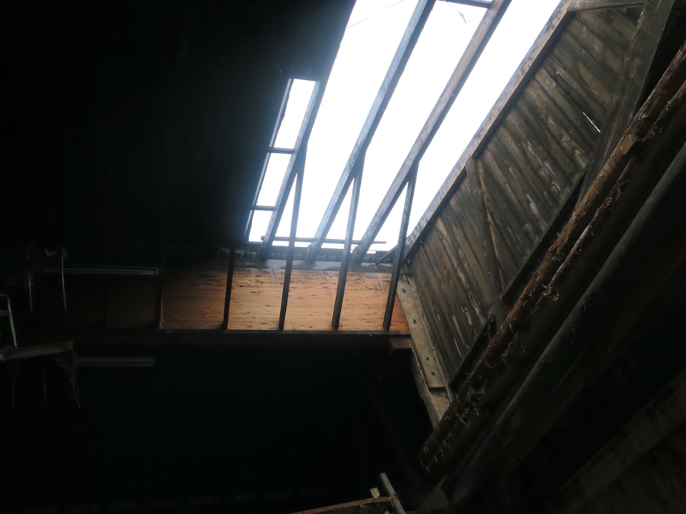 Ein Dach, bei dem Ziegel fehlen, aus dem Gebäude-Innern fotografiert.