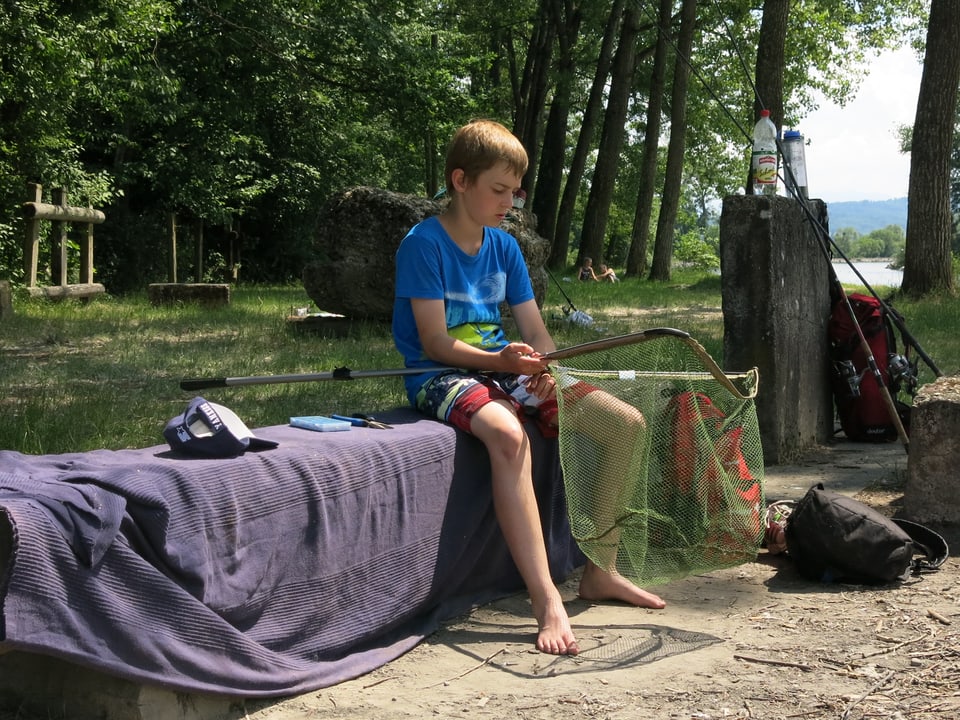 Ein junger Teilnehmer sitzt auf einem Baumstamm und hält ein Fischernetz in der Hand. 