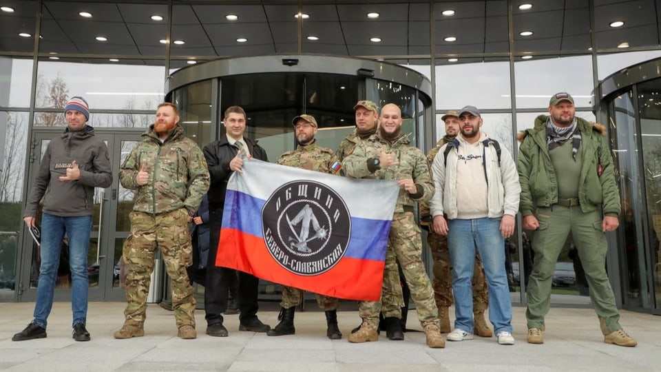 Besucher posieren gemeinsam mit Männern in Militäruniform für ein Foto vor dem PMC Wagner Center.
