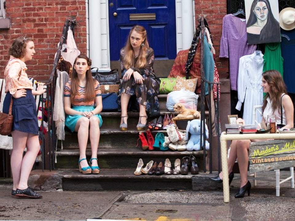 Die Girls sitzen vor einer Haustür, wo sie einen Trödelmarkt veranstalten.