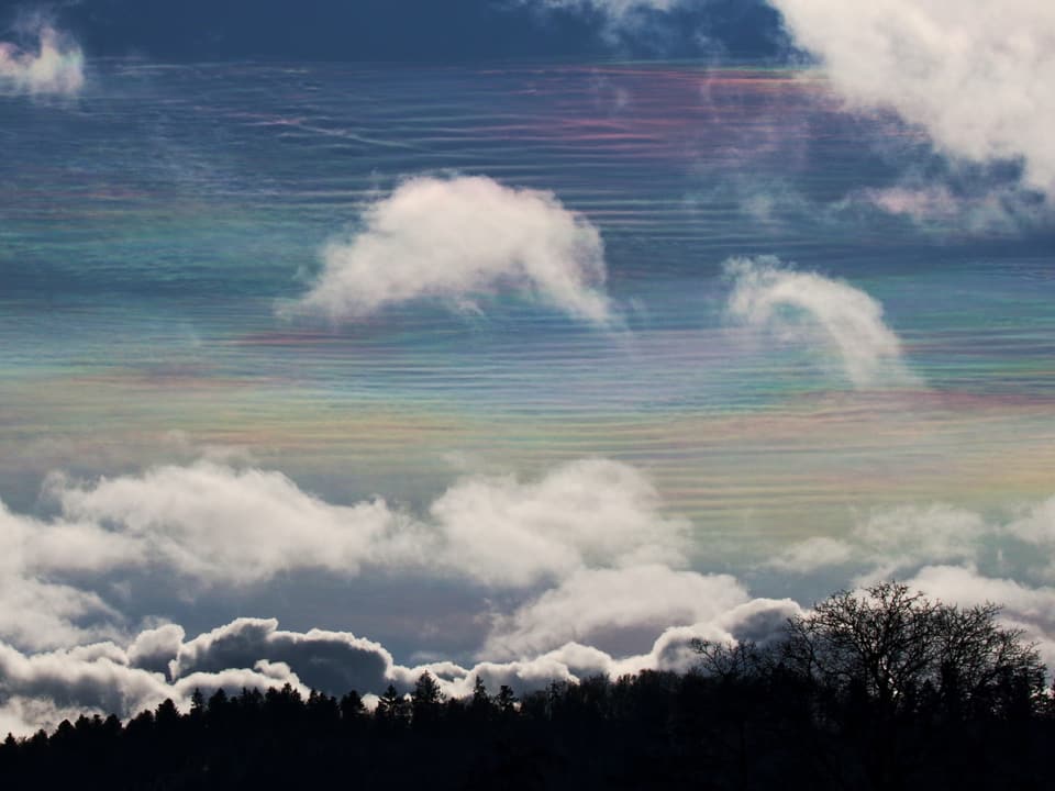 In Richtung Süden zeigen sich Irisierende Wolken. Die streifenartigen dünnen hohen Wolkenfelder weisen Regenbogenfarben auf. Im Vordergrund hat es weisse kleine Quellwolken.