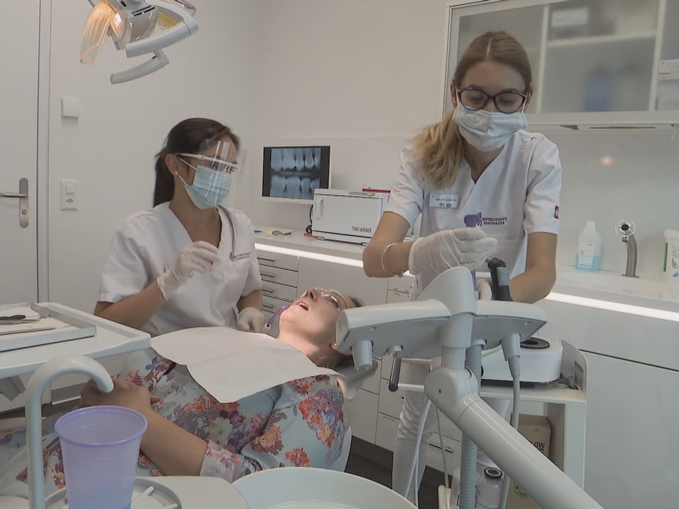 Zwei Dentalhygienikerinnen arbeiten in einer Praxis. Zwischen ihnen liegt eine Patientin.