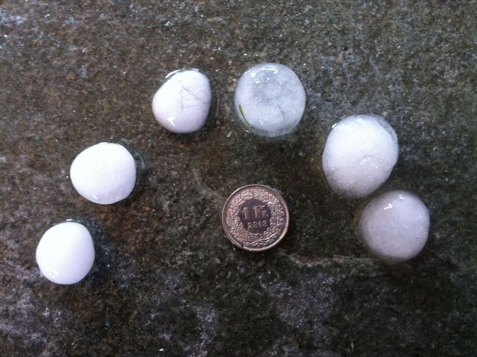Schwarzer Hintergrund mit 1 Frankenstück und 6 Hagelkörnen in der selben Grösse. 