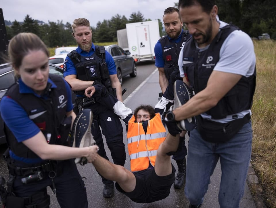 Polizisten tragen einen Klimaaktivist mit Warnweste von der Strasse weg.