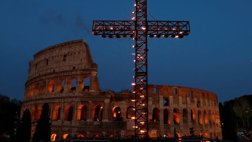 Totale auf das Kolosseum in Rom mit einem Kreuz im Vordergrund.