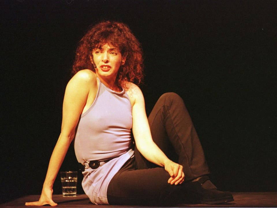 Die US-amerikanische Sängerin, Komponistin und Performerin Shelley Hirsch, auf der Bühne auf dem Boden sitzend.