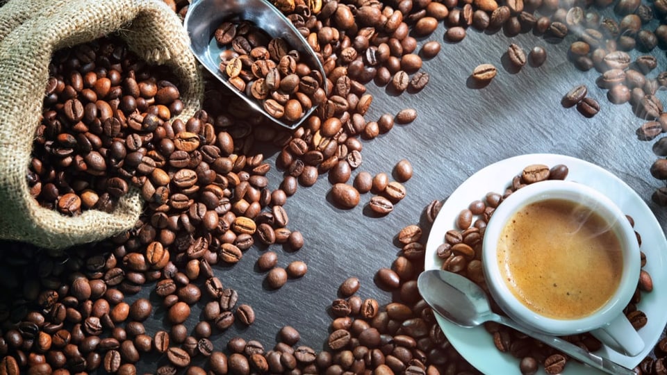 Eine Tasse Espresso mit Schaum neben vielen Kaffeebohnen und einem Leinensack