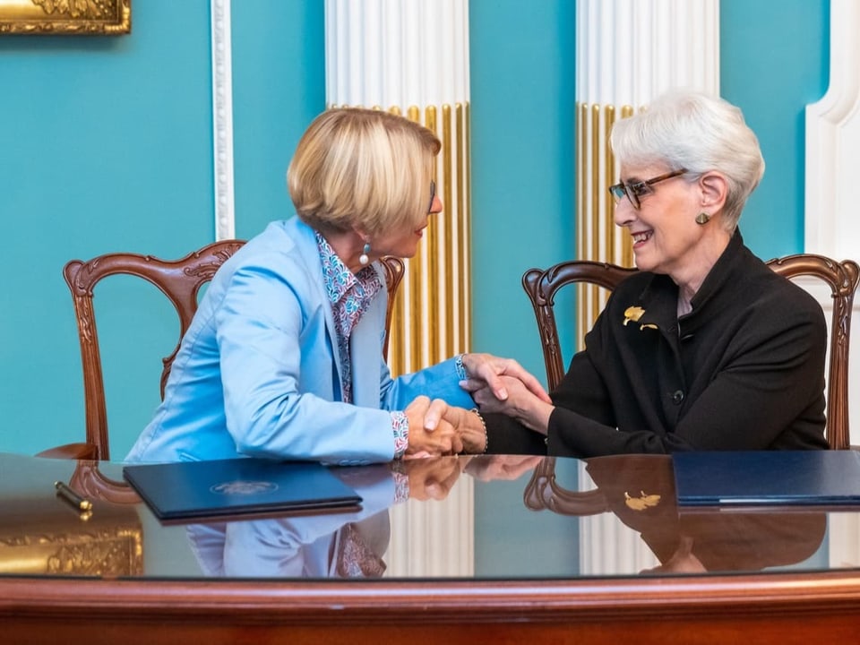 Livia Liu and Sandy Sherman shake hands.  There are documents lying on the table in front of them.